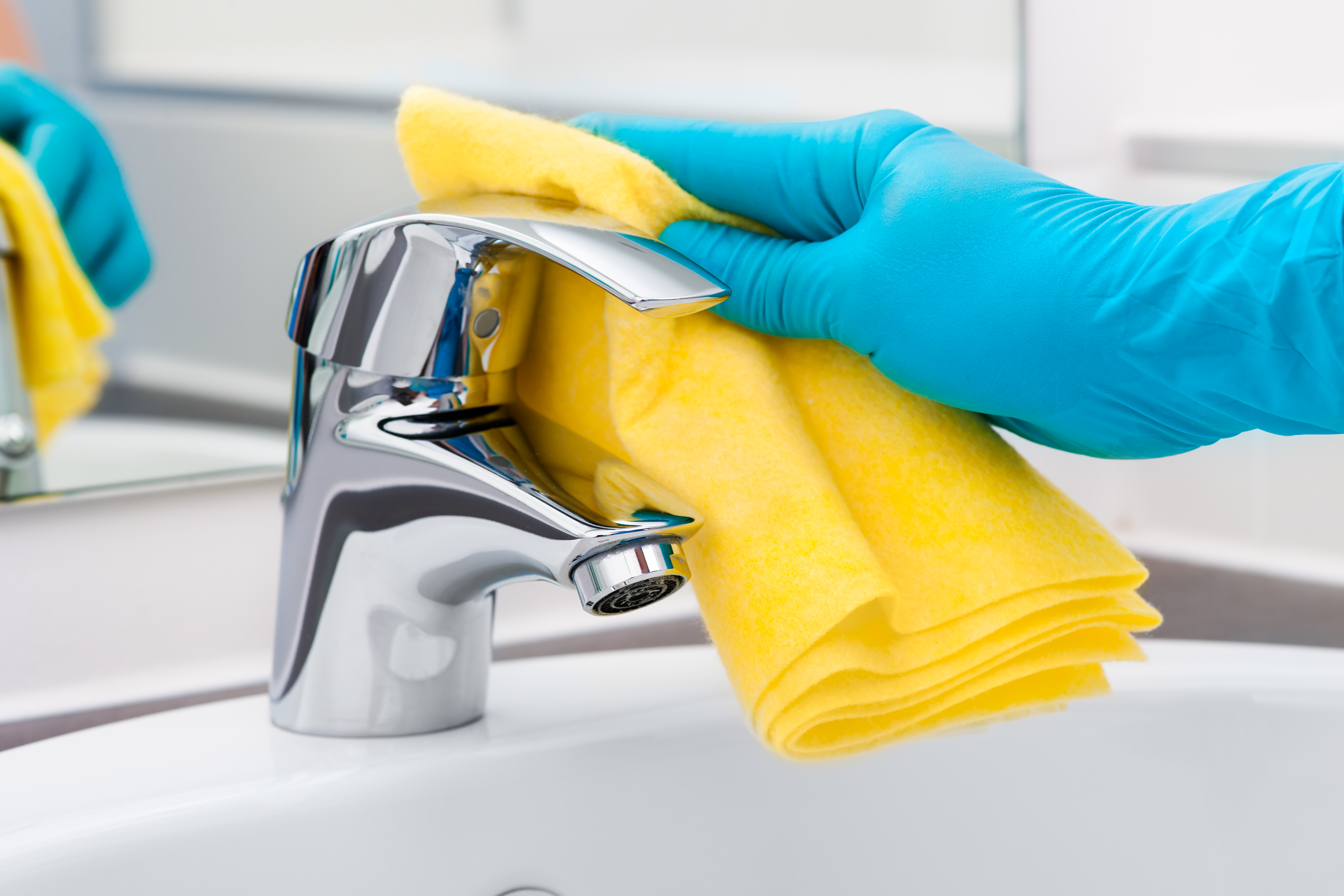Cleaning a bathroom faucet with a yellow cloth, as shown on CleanScene Miami’s official website